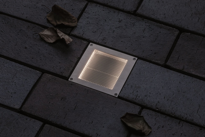 Un éclairage de sol encastré allumé sur des pavés sombres.