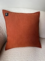 Ein orangefarbenes Heizkissen auf einem Sofa.