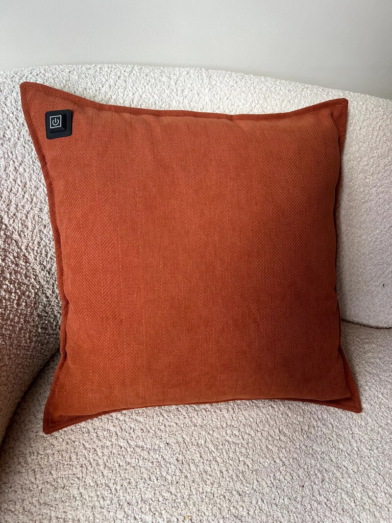 Ein orangefarbenes Heizkissen auf einem Sofa.
