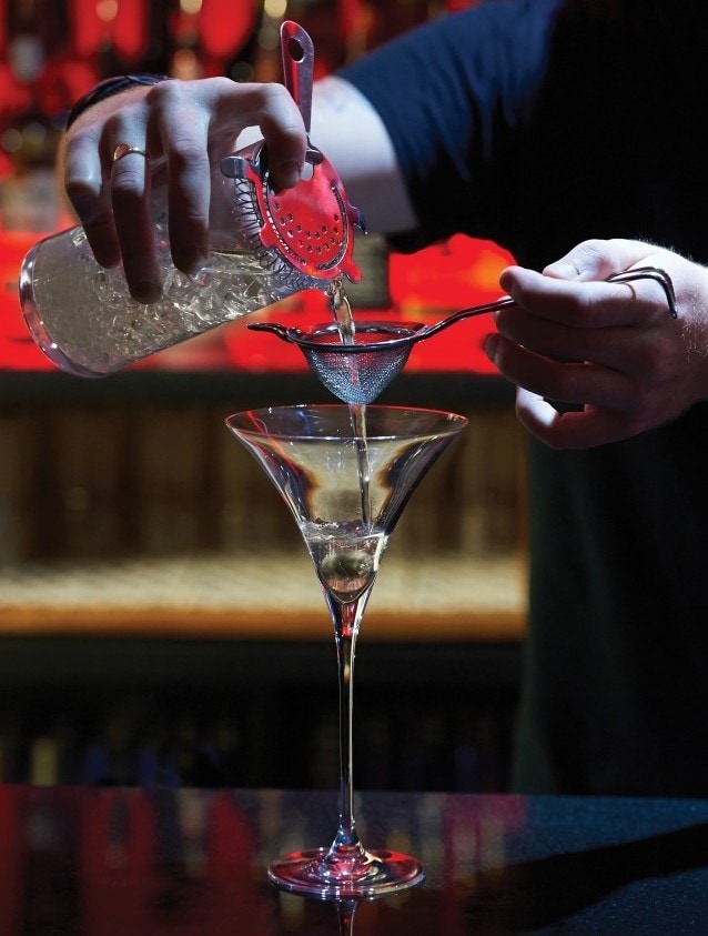 Um barman coa um cocktail através de um coador.