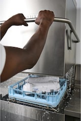 Um homem usa uma máquina de lavar louça industrial.