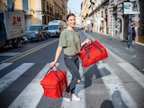 Una mujer cruza la calle con dos bolsas rojas.