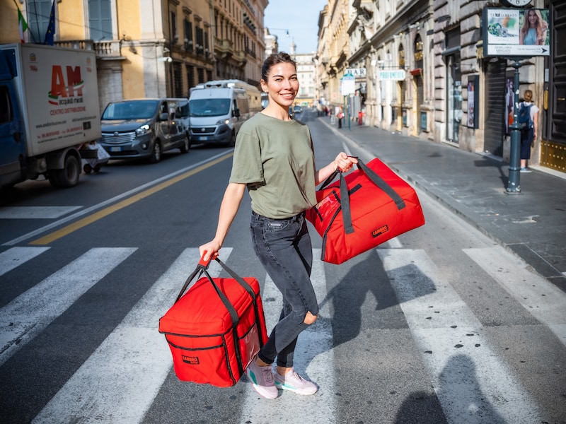 Una mujer cruza la calle con dos bolsas rojas.