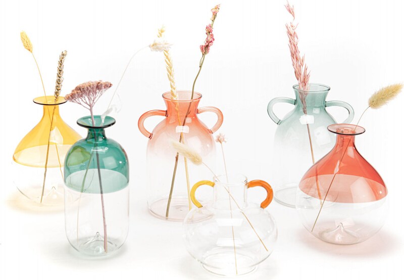 Sechs bunte Glasvasen mit Trockenblumen.