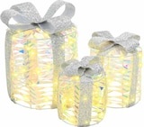 Drei beleuchtete Geschenkboxen mit silbernen Schleifen.