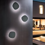 Drei dunkle, runde Wandleuchten beleuchten eine Wand.