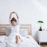 Frau streckt sich im Bett, Nachttischlampe daneben.