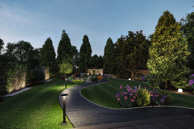 Beleuchteter Gartenweg mit Bäumen und Blumen.