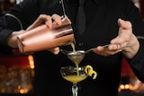 Um barman coa um cocktail através de um coador.