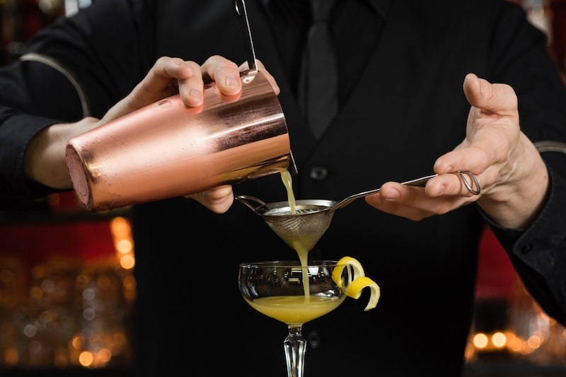 Um barman coa um cocktail através de um coador.