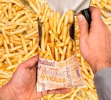 Uma pessoa enche um saco de papel com batatas fritas.