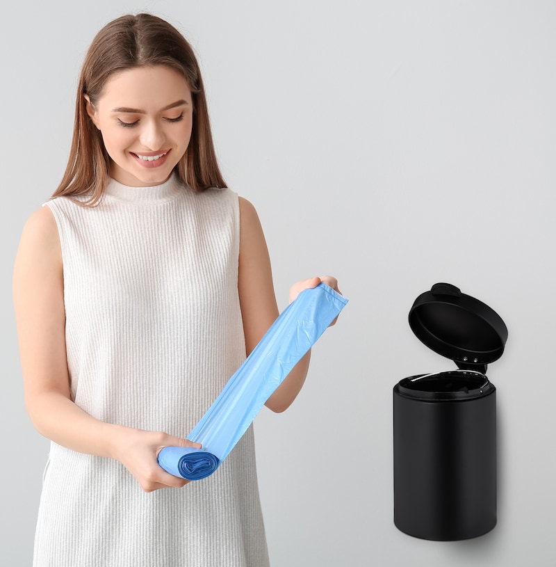 Frau hält blaue Müllbeutel neben einem Mülleimer.