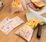 Batatas fritas em sacos de papel sobre mesa de madeira.