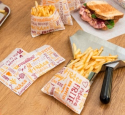 Batatas fritas em sacos de papel sobre mesa de madeira.