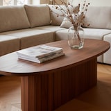 Une table ovale en bois avec magazines et vase.