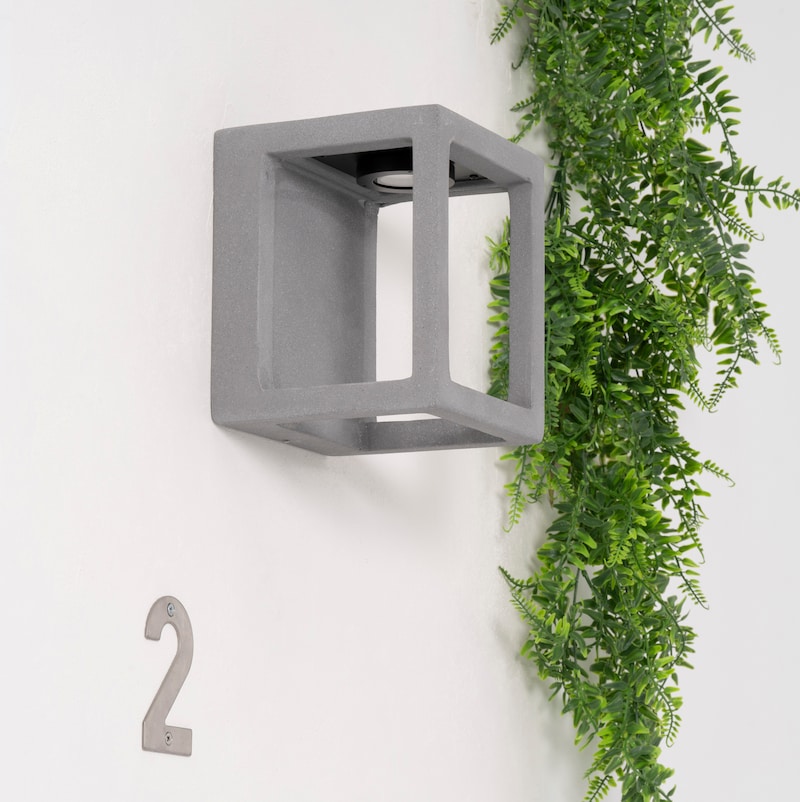 Aplique de pared gris en forma de cubo junto a una planta.
