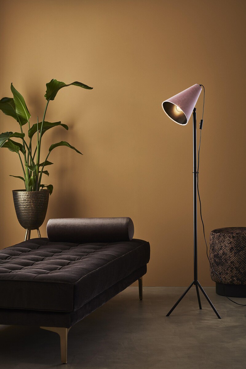 Ein rosafarbener Stehlampe neben einem Sofa.