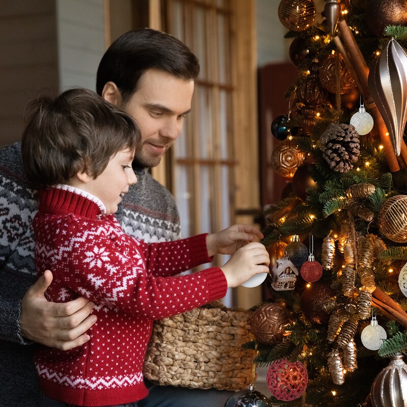 Ein Mann und ein Kind schmücken einen Weihnachtsbaum.