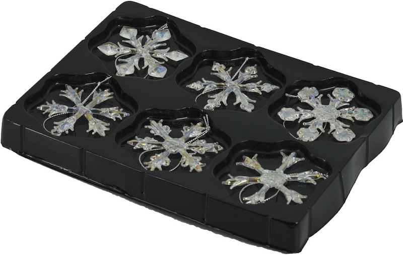 Sei scintillanti ornamenti a fiocco di neve in un vassoio nero.